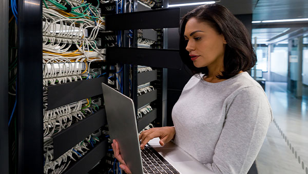A woman holding a laptop while checking on a server in a data center